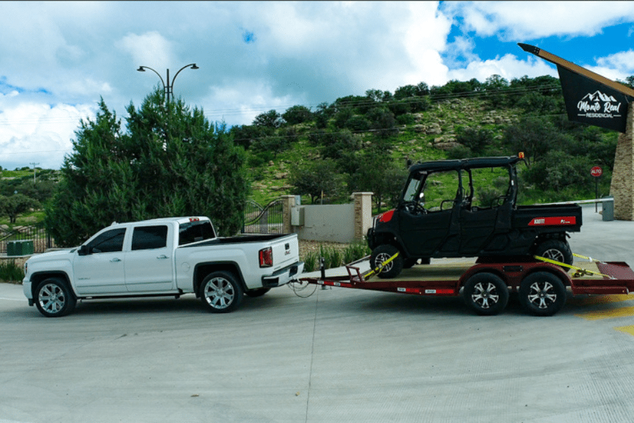 white truck hauling black golf cart on red flatbed arrow trail trailer